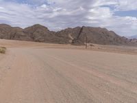 an empty dirt road between large mountain range and a grassy plain with gravel floor and grass in foreground