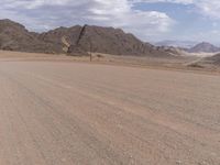 an empty dirt road between large mountain range and a grassy plain with gravel floor and grass in foreground