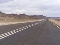 an empty highway in the desert with hills in the background and a yellow bus on it's lane