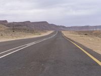 an empty highway in the desert with hills in the background and a yellow bus on it's lane