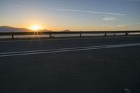 a photo taken of the sun on the road at sunrise time in front of mountains