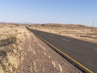 an empty highway surrounded by tall grass and mountains in the distance, looking toward the horizon