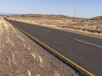 an empty highway surrounded by tall grass and mountains in the distance, looking toward the horizon