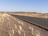 an empty highway surrounded by tall grass and mountains in the distance, looking toward the horizon