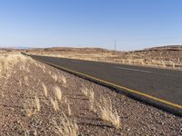 an empty highway surrounded by tall grass and mountains in the distance, looking toward the horizon