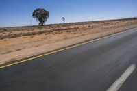 a motorcycle riding on a desert road through the middle of nowhere, with dry bushes around