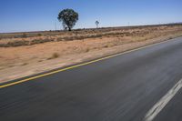 a motorcycle riding on a desert road through the middle of nowhere, with dry bushes around