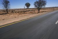 a motorcycle riding on a desert road through the middle of nowhere, with dry bushes around