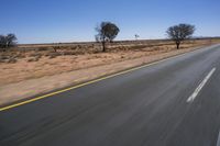 a motorcycle riding on a desert road through the middle of nowhere, with dry bushes around