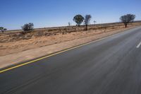 a motorcycle riding on a desert road through the middle of nowhere, with dry bushes around