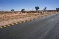 a motorcycle riding on a desert road through the middle of nowhere, with dry bushes around