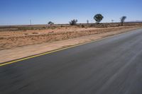 a motorcycle riding on a desert road through the middle of nowhere, with dry bushes around