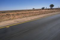 a motorcycle riding on a desert road through the middle of nowhere, with dry bushes around