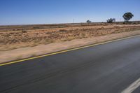 a motorcycle riding on a desert road through the middle of nowhere, with dry bushes around