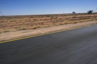 a motorcycle riding on a desert road through the middle of nowhere, with dry bushes around