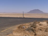 a stop sign on the side of a road in the desert, in front of a hill and road lined by sand