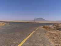 a stop sign on the side of a road in the desert, in front of a hill and road lined by sand