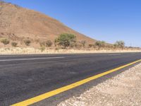 the empty road is next to the mountains in the distance and a lone yellow stripe on the ground