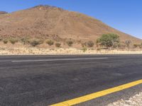 the empty road is next to the mountains in the distance and a lone yellow stripe on the ground