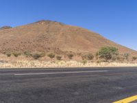 the empty road is next to the mountains in the distance and a lone yellow stripe on the ground