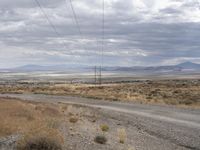 an intersection with a road and power lines over it with a dirt road and mountains beyond