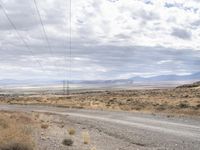 an intersection with a road and power lines over it with a dirt road and mountains beyond