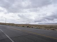 a empty road in an open desert field with cloudy skies above it and the street light on the far side