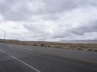 a empty road in an open desert field with cloudy skies above it and the street light on the far side