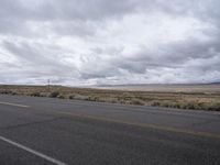 a empty road in an open desert field with cloudy skies above it and the street light on the far side