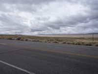 a empty road in an open desert field with cloudy skies above it and the street light on the far side