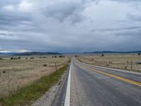 a long street passes a prairie area and mountains in the distance with heavy clouds in the sky