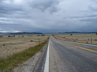 a long street passes a prairie area and mountains in the distance with heavy clouds in the sky