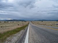 a long street passes a prairie area and mountains in the distance with heavy clouds in the sky