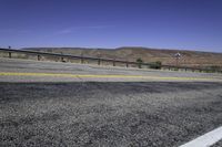 two yellow lines are on the road beside a fence and mountains in the distance of the photo