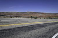 two yellow lines are on the road beside a fence and mountains in the distance of the photo