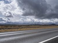 an open highway on a cloudy day with snow covered mountains in the distance and two people on the side