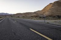 a lone road with no people on it in the desert area at dusk, looking out toward a mountainous landscape