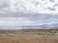 power lines stretching across the desert toward the horizon of the distant field and distant land