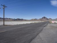 a picture of a city road in the desert with no cars on it that is blocked by power lines and telephone poles