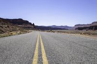 two white double parallel lines on a road in the desert, with mountains in the distance