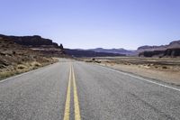 two white double parallel lines on a road in the desert, with mountains in the distance