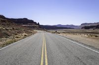 two white double parallel lines on a road in the desert, with mountains in the distance