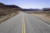 two white double parallel lines on a road in the desert, with mountains in the distance