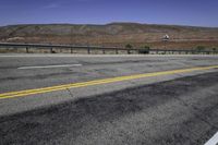 a very wide empty highway with mountains in the distance as seen from a street corner