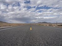 an empty highway in the middle of nowhere with mountains in the background and a cloudy sky overhead