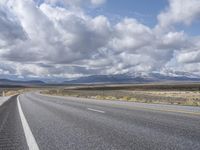 an empty highway in front of mountains under a blue sky filled with clouds during the day