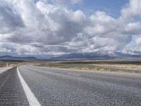 an empty highway in front of mountains under a blue sky filled with clouds during the day