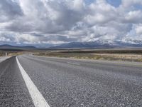 an empty highway in front of mountains under a blue sky filled with clouds during the day