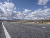 an empty highway in front of mountains under a blue sky filled with clouds during the day