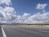 an empty highway in front of mountains under a blue sky filled with clouds during the day